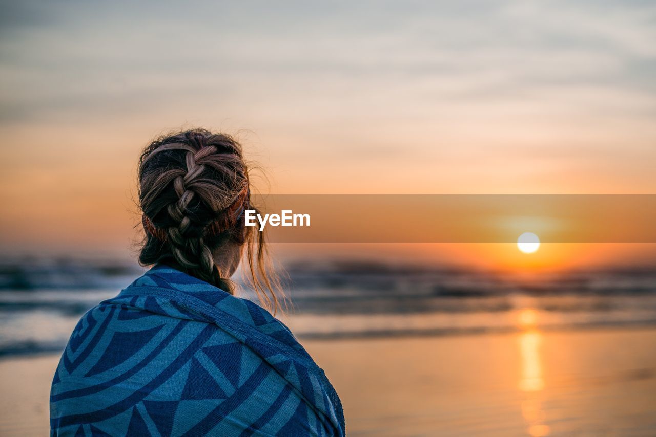 Rear view of woman against sea during sunset