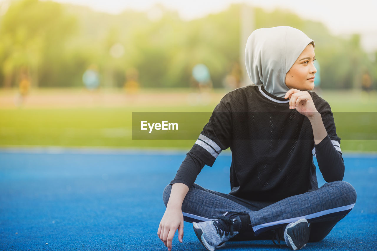 Thoughtful female athlete sitting at stadium