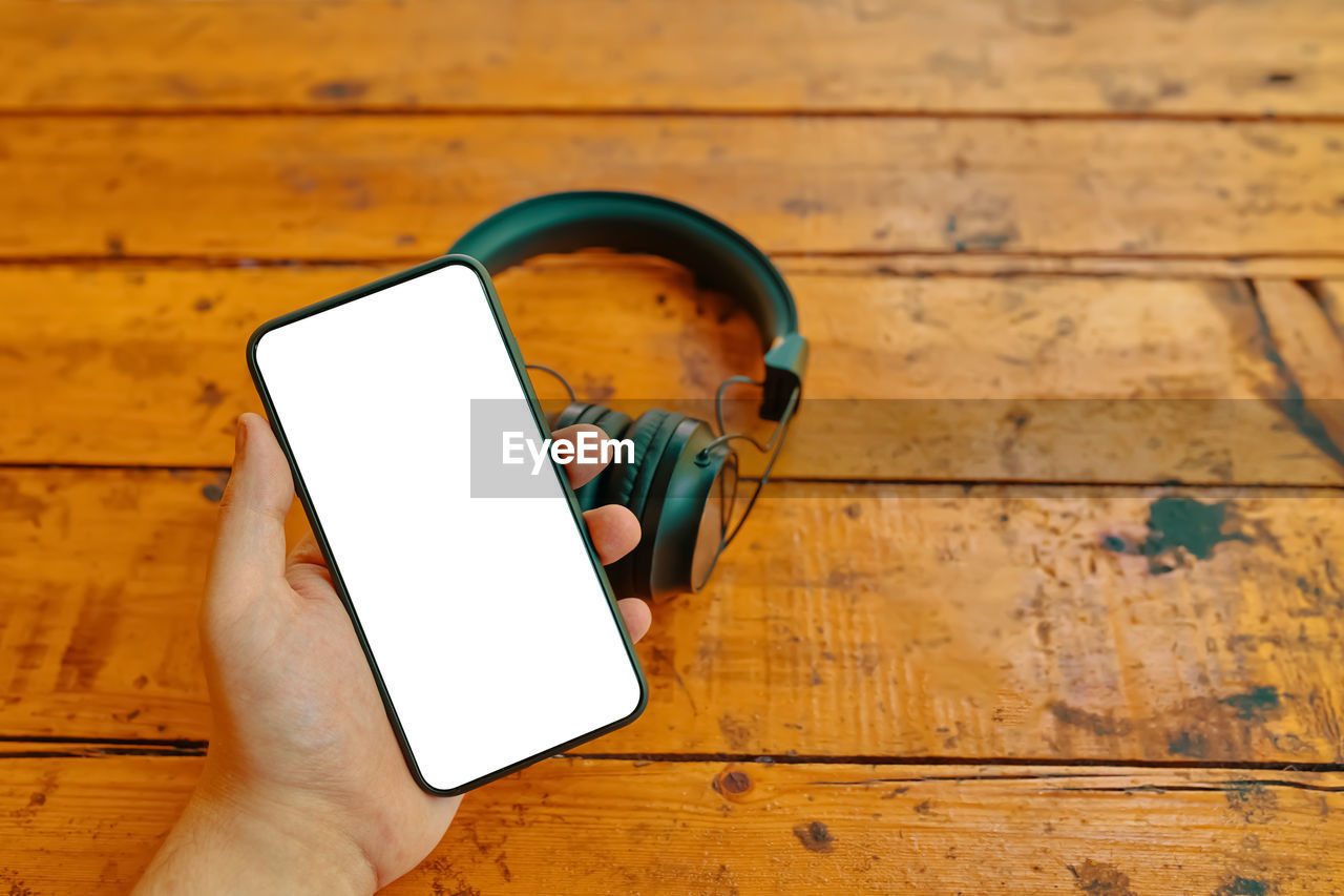 HIGH ANGLE VIEW OF HAND HOLDING MOBILE PHONE ON TABLE