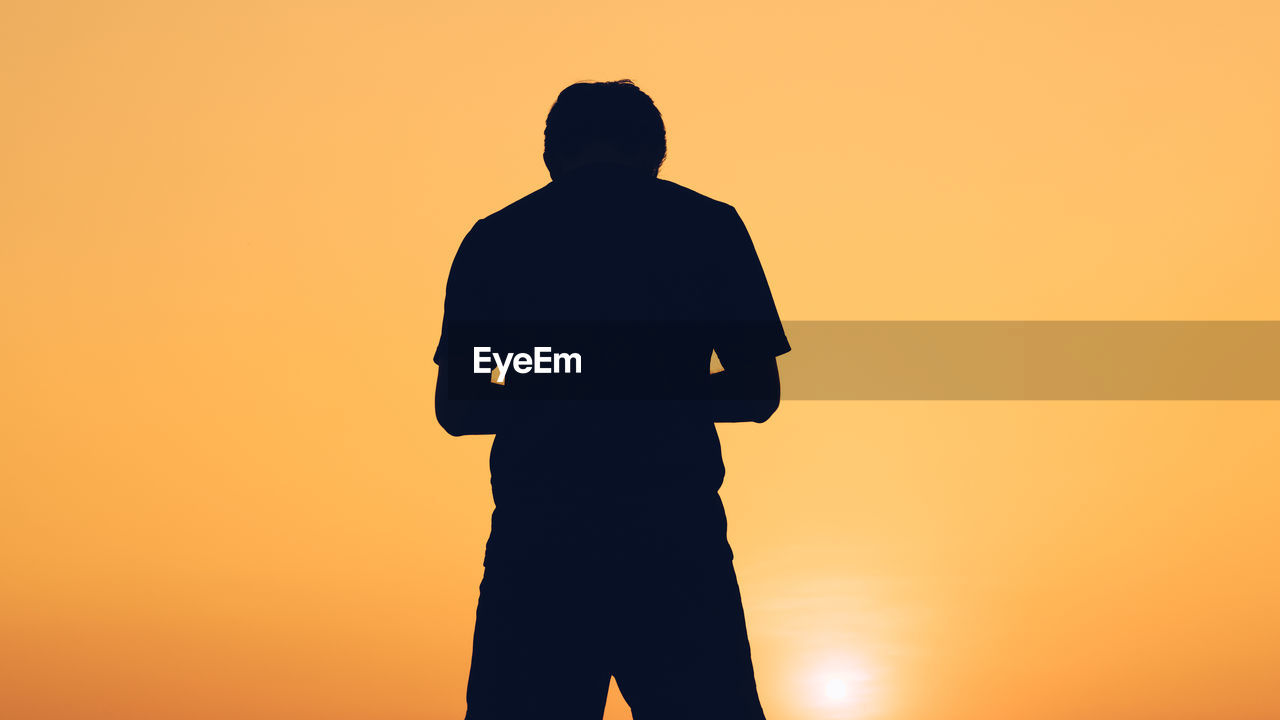 REAR VIEW OF SILHOUETTE MAN STANDING AGAINST SKY DURING SUNSET