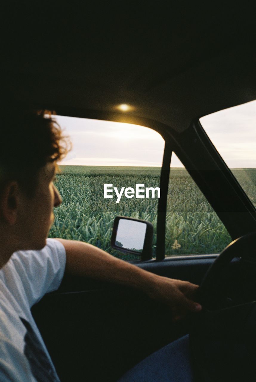 Man sitting in old car watching sunset 