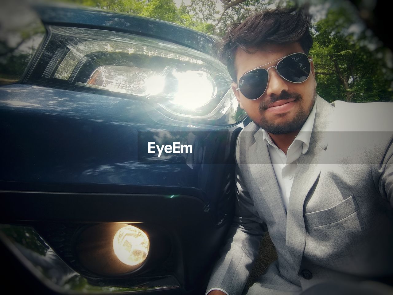 Portrait of young man wearing sunglasses by illuminated headlight of car