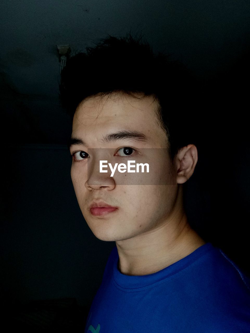 Close up portrait of young handsome asian male wears casual blue shirt against black background