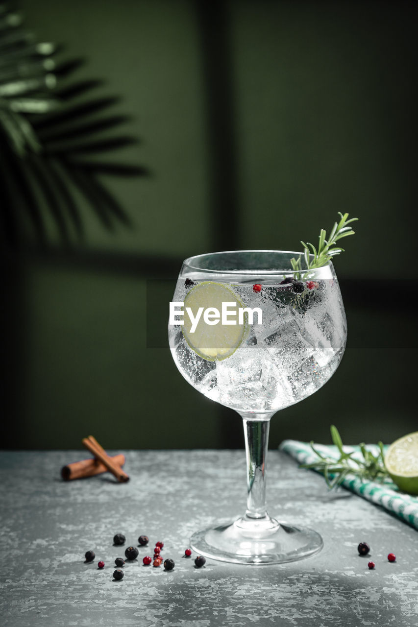 Gin tonic cocktail and shadows next to the window on dark concrete background. vertical format.