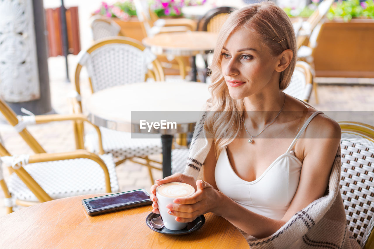 young woman using mobile phone while sitting at cafe