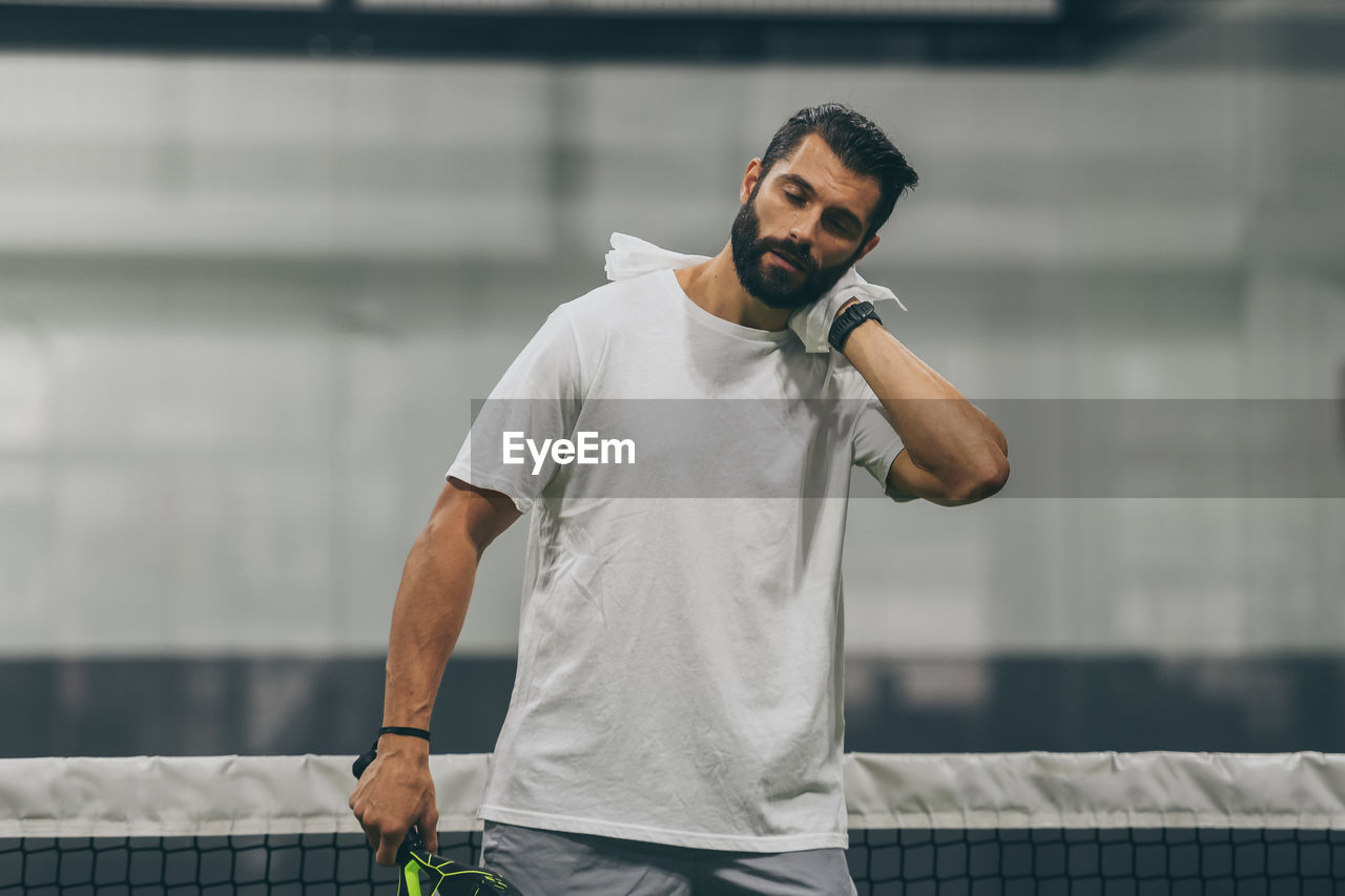 Beautiful man playing paddle tennis, racket in hand wipes the sweat. young sporty boy after match. 