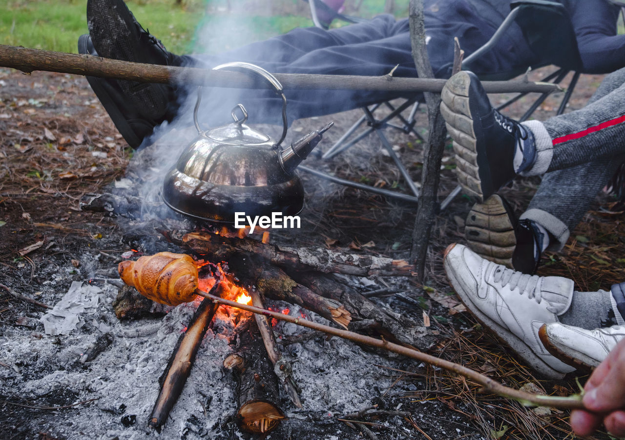 Young and cheerful friends sitting at bonfire , boil the kettle and fry bread on the nature. cooking