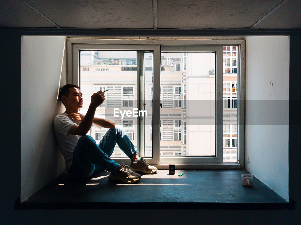 Young man smoking cigarette while sitting by window at home