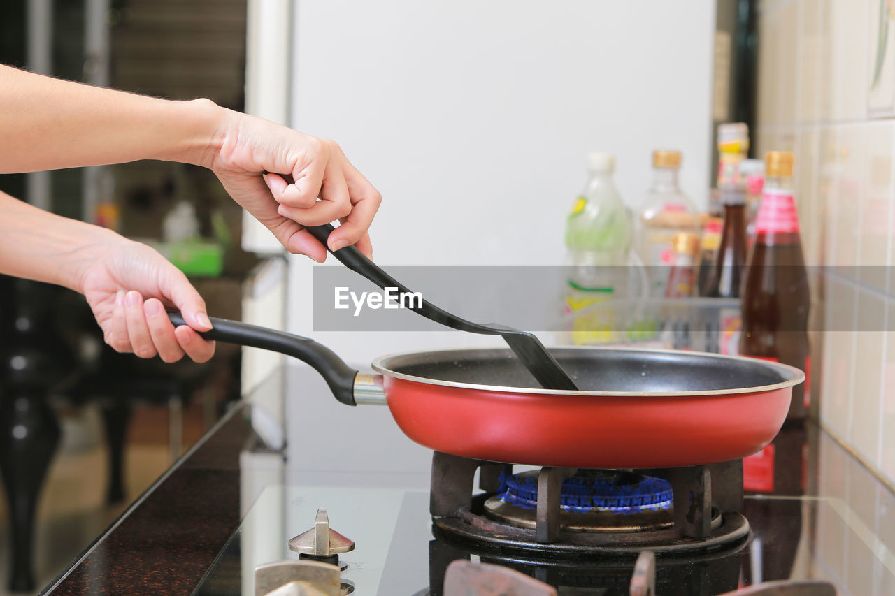 Cropped hands of woman frying food in kitchen