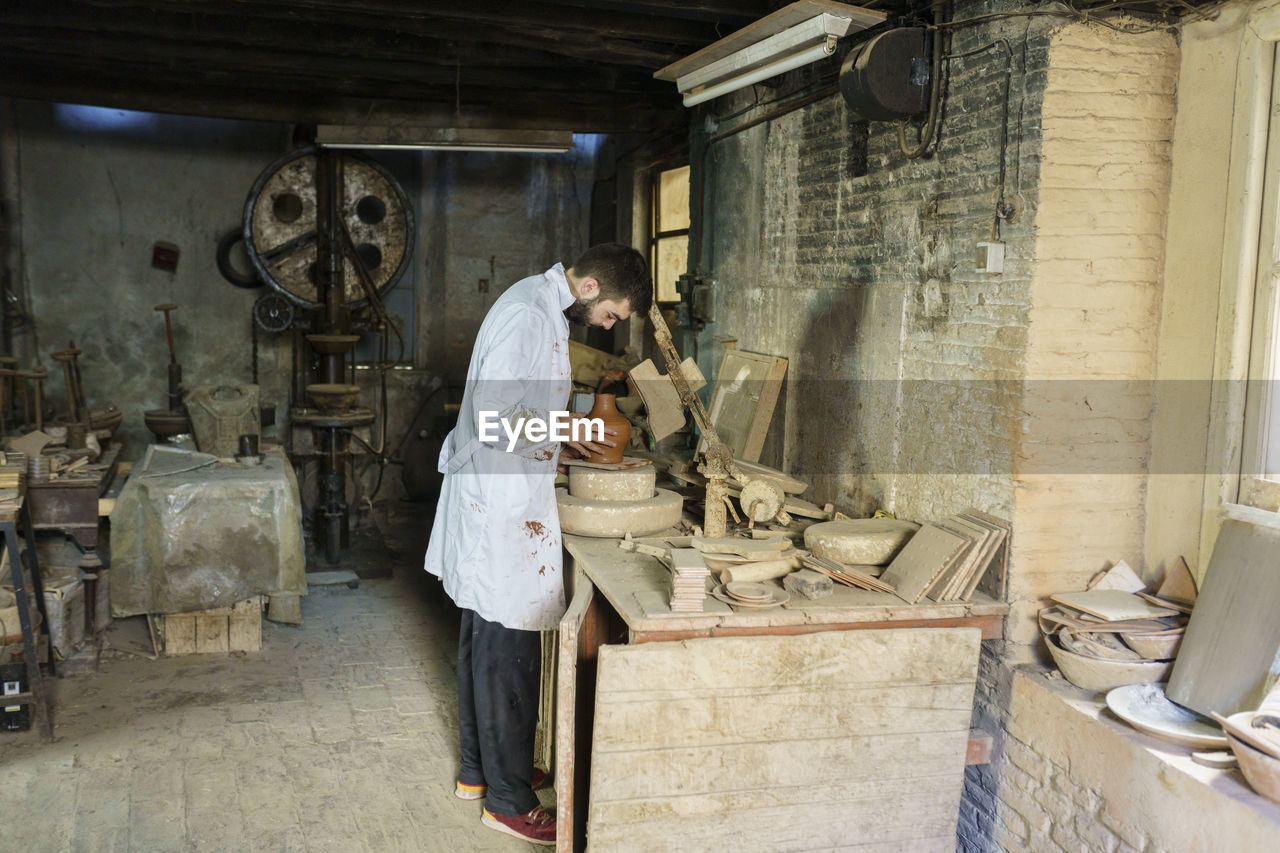 Craftsman examining ceramic pot standing at workbench in factory