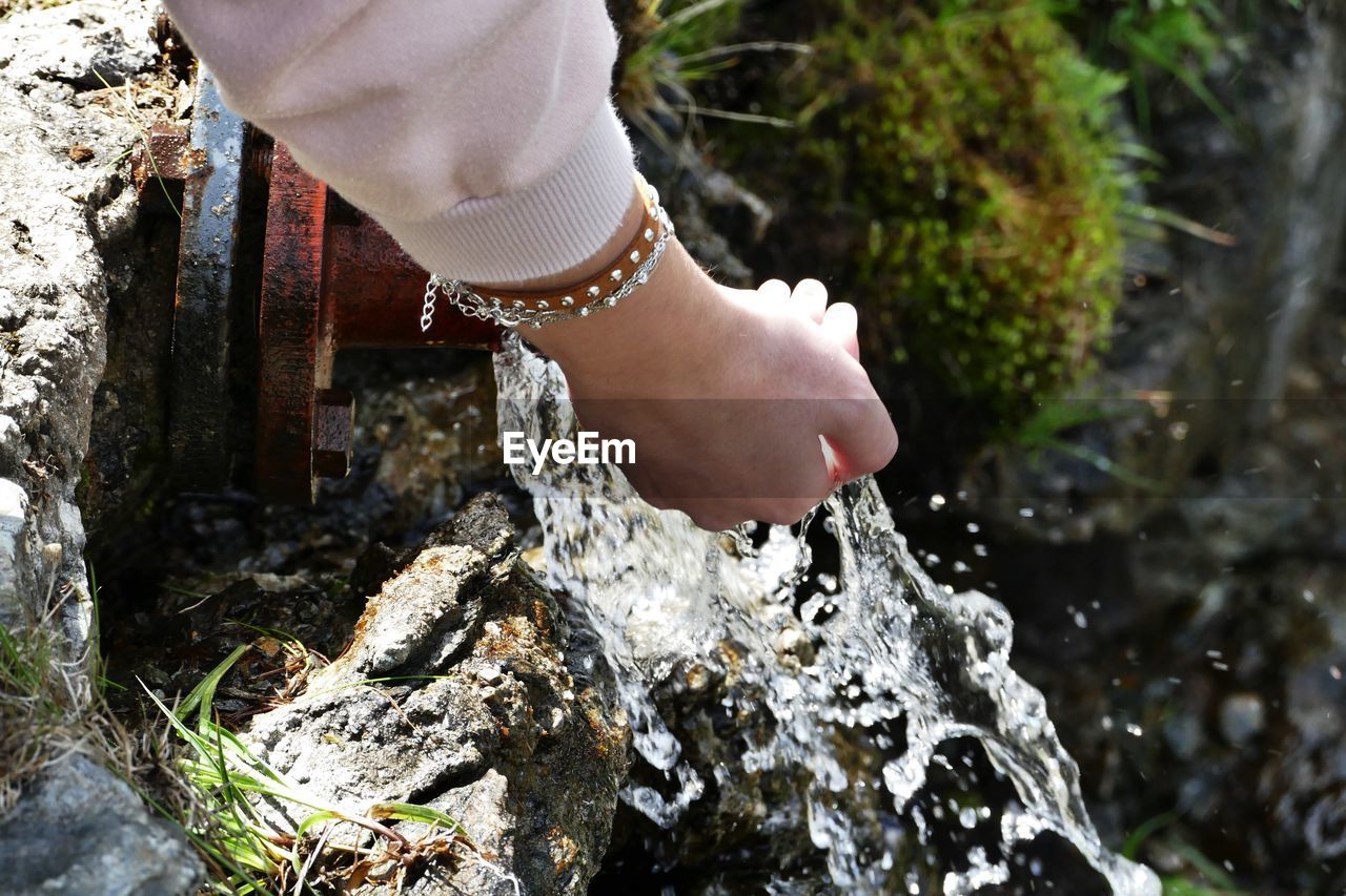 Cropped hand of woman collecting water from pipe