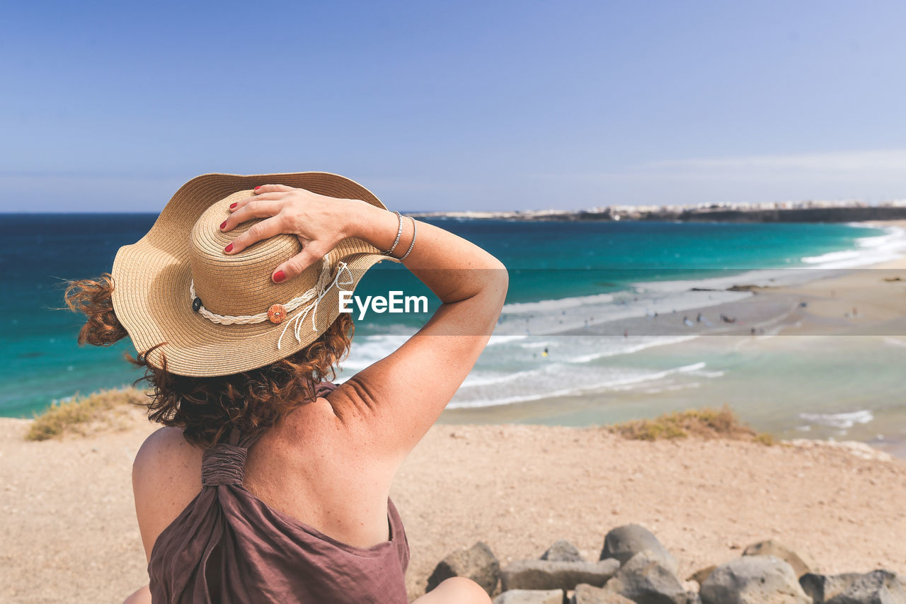 Rear view of woman wearing hat at beach against sky