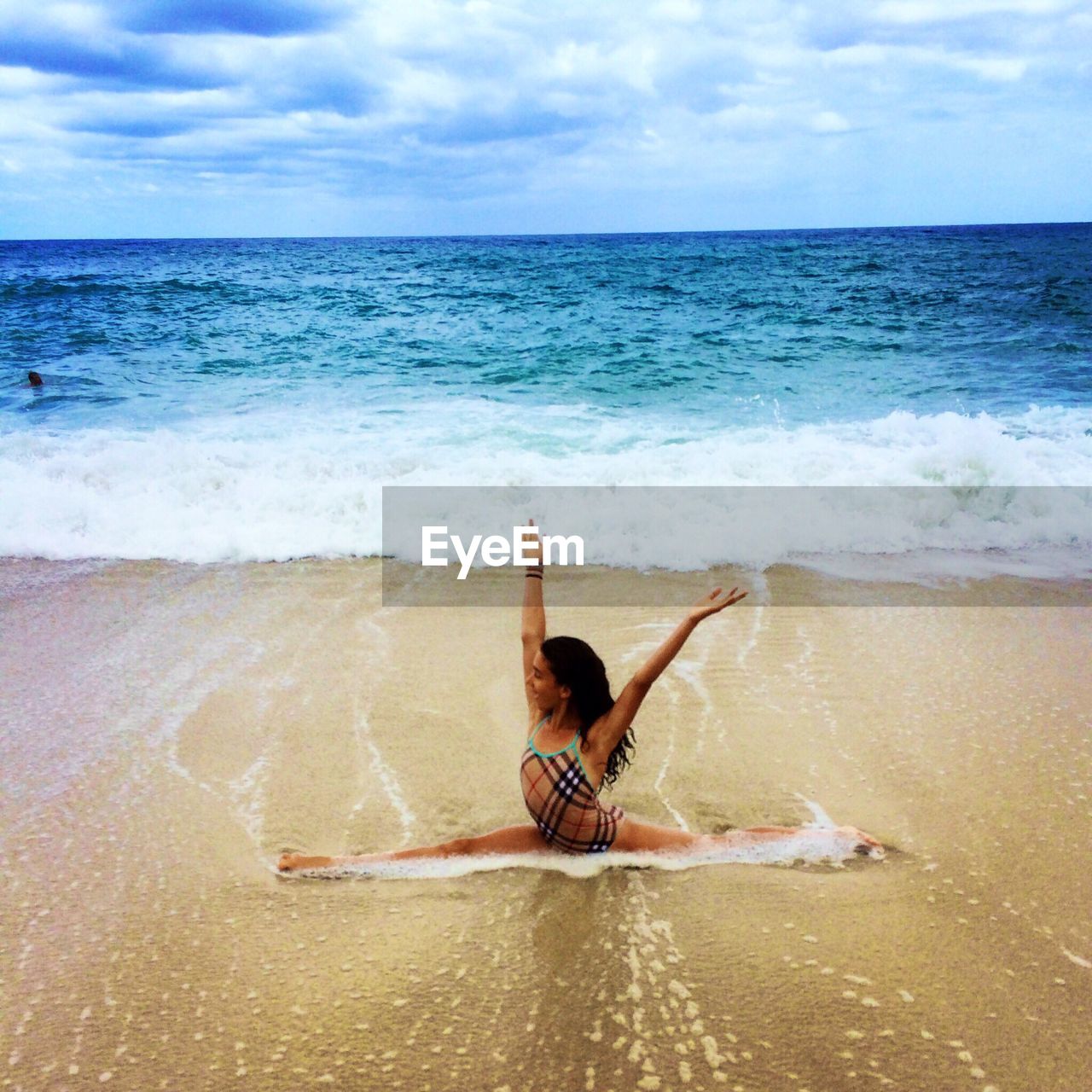 Young woman stretching on sea shore with arms raised