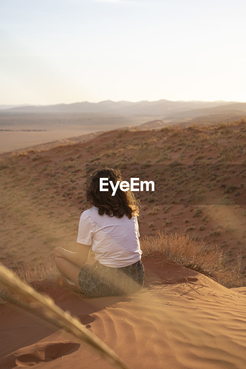 Rear view of woman sitting on sand