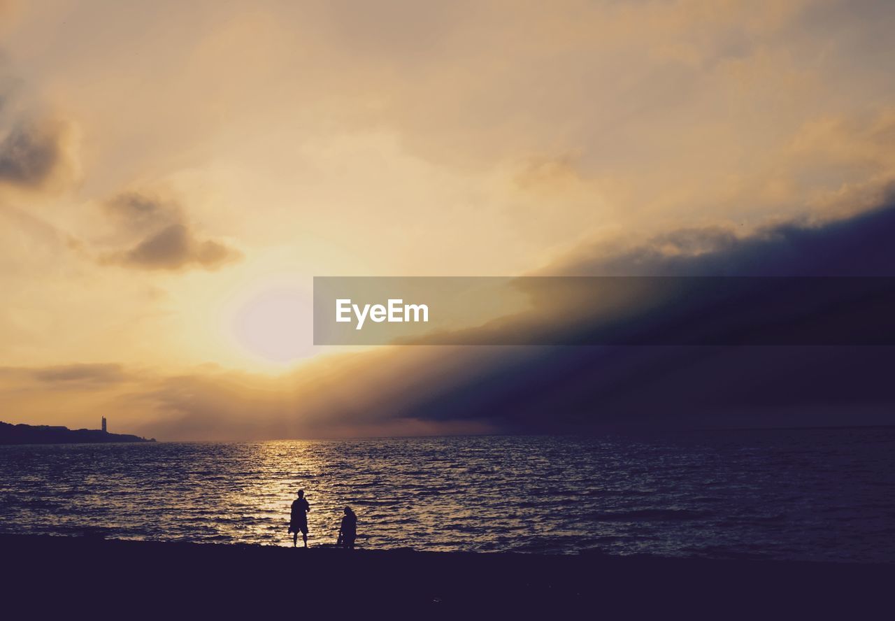 SILHOUETTE MAN STANDING AT BEACH DURING SUNSET