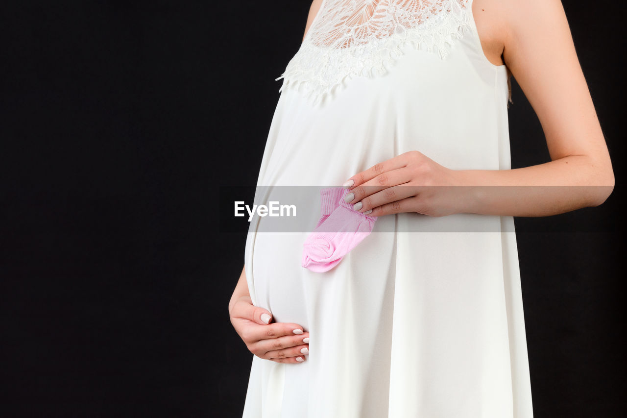 MIDSECTION OF WOMAN HOLDING HANDS AGAINST WHITE BACKGROUND