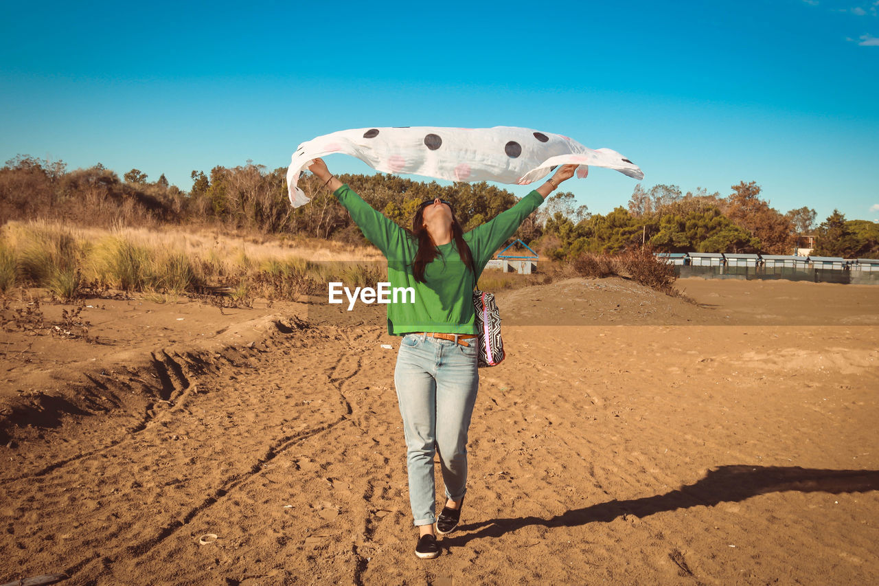 Full length of woman holding scarf while standing on sand