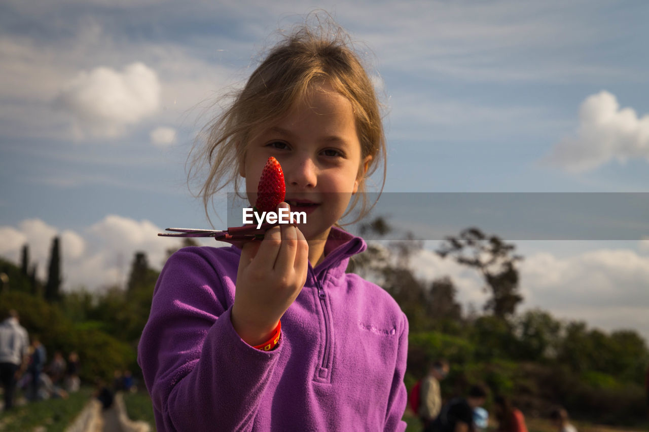 Portrait of cute smiling girl holding strawberry and scissors at farm