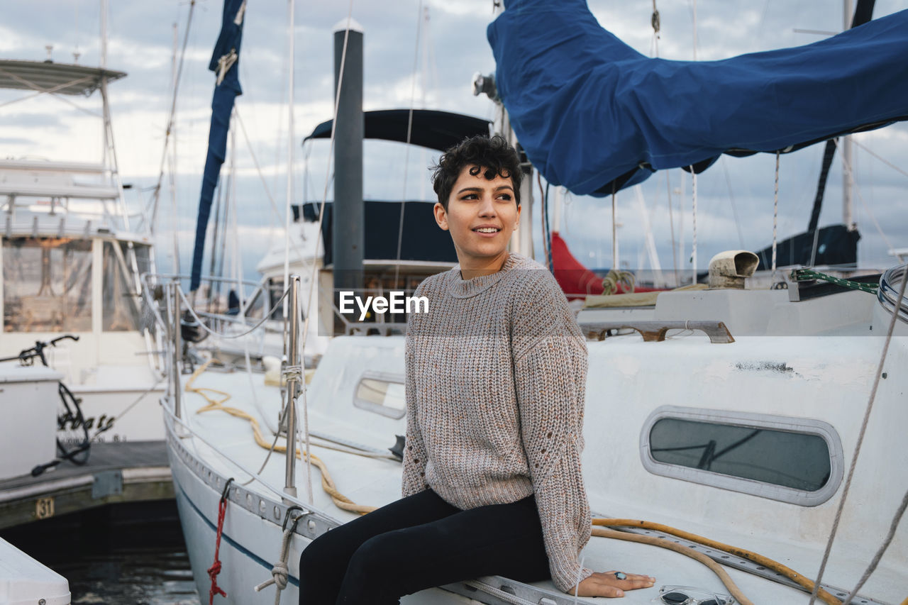 Thoughtful woman looking away while sitting on boat against cloudy sky during sunset