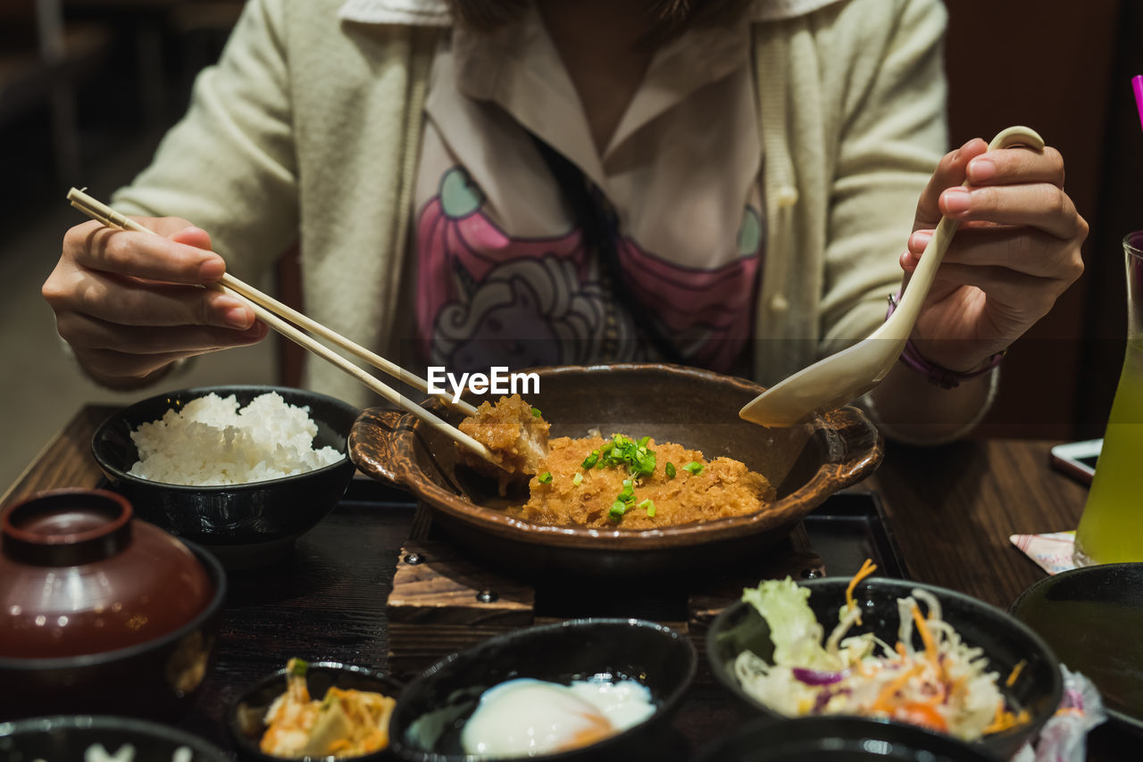 Close-up midsection of woman having meal with chopsticks at table