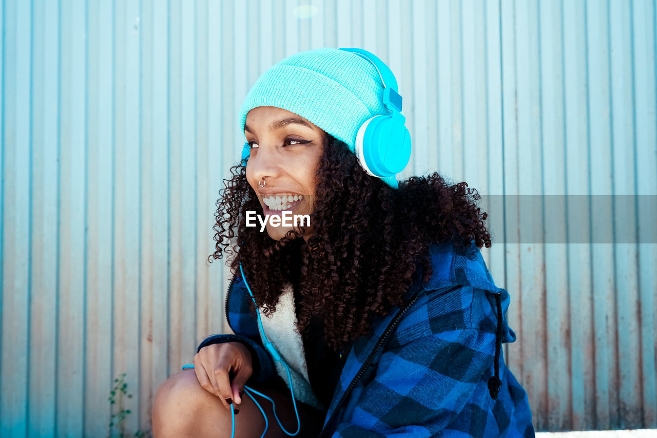 Happy young woman listening to music on headphones against closed shutter