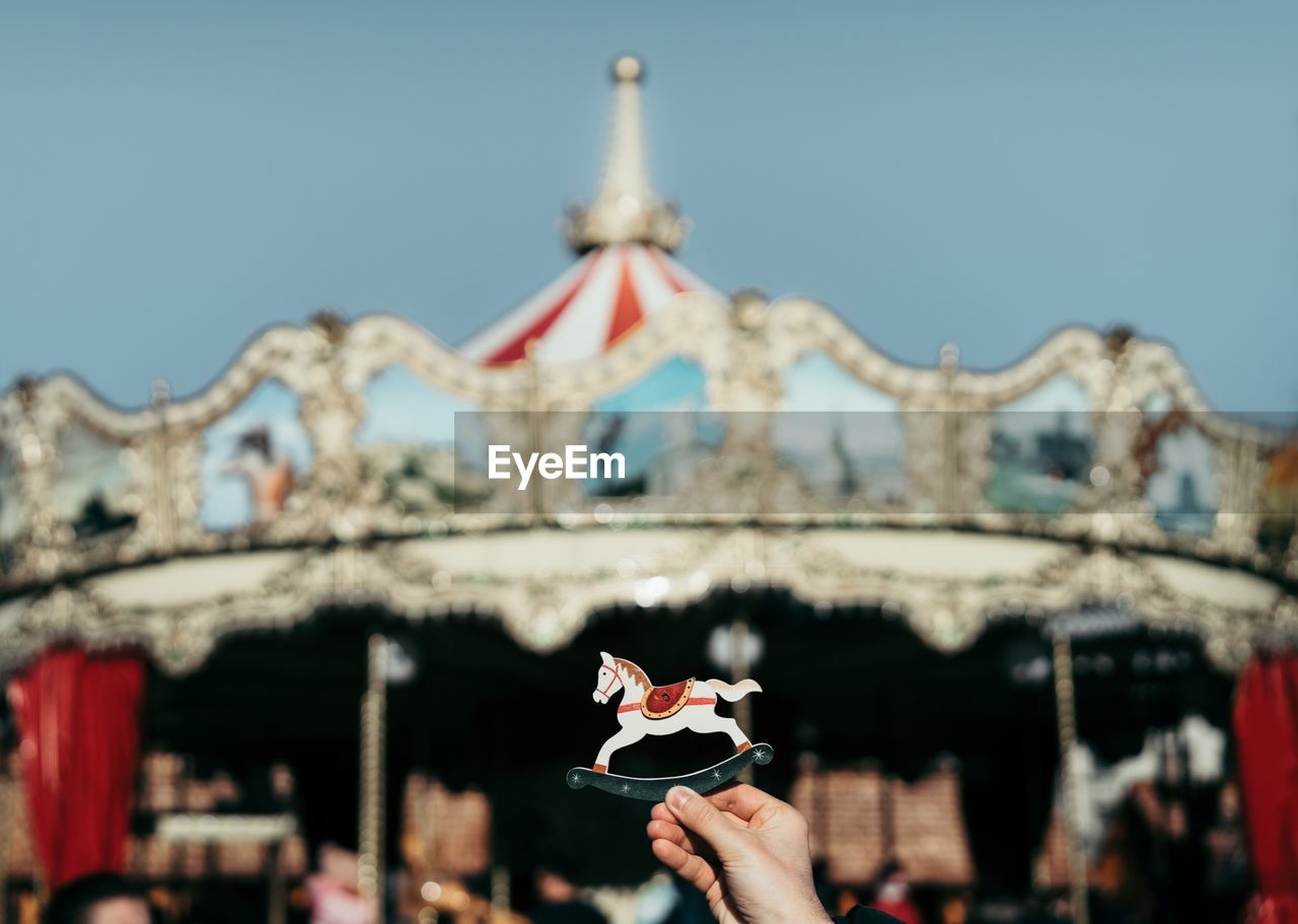 Close-up of hand holding toy against carousel 