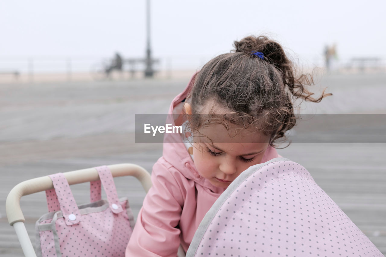 Young girl playing with her toy stroller on the boardwalk