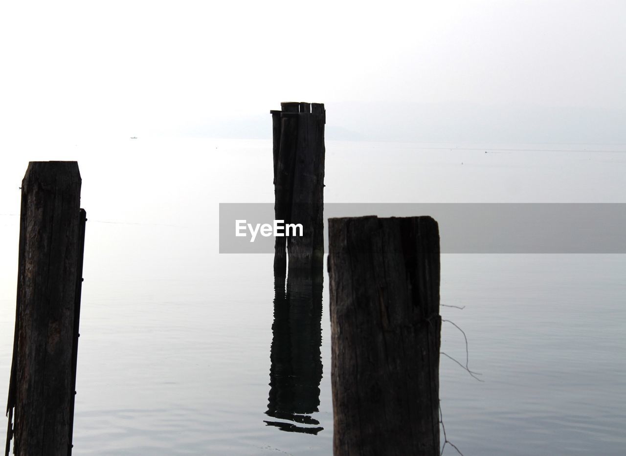 Wooden posts in calm lake against sky