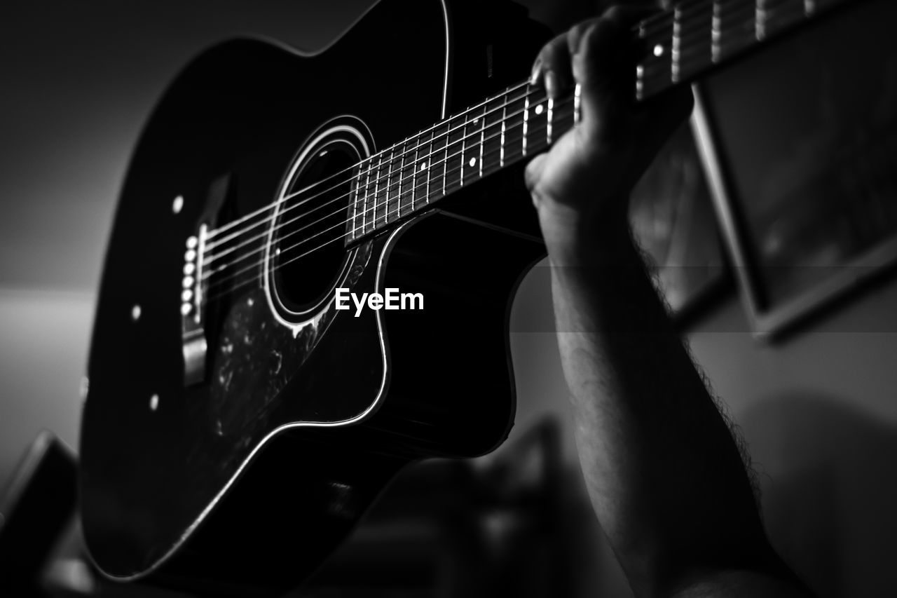 Cropped hand of man holding guitar at home