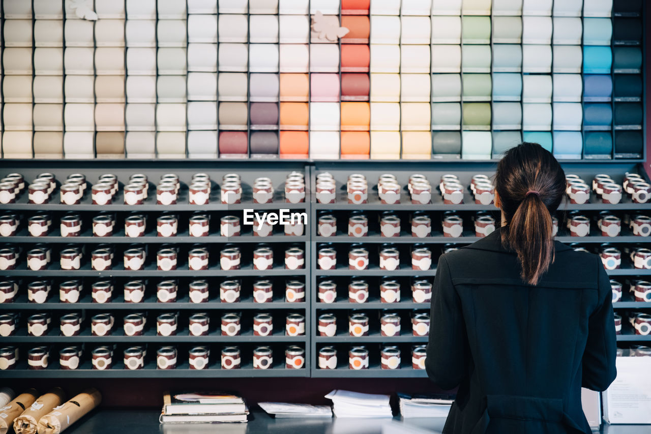 Rear view of woman choosing wallpapers and paints displayed for sale in store