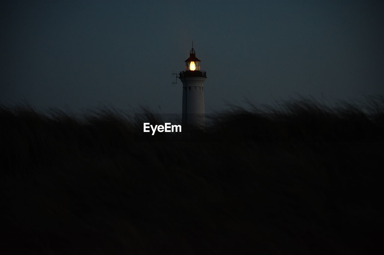 Lighthouse by silhouette building against sky at dusk