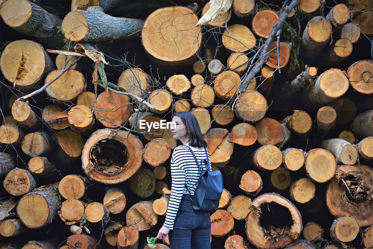 Rear view of woman with backpack standing by woodpile in forest