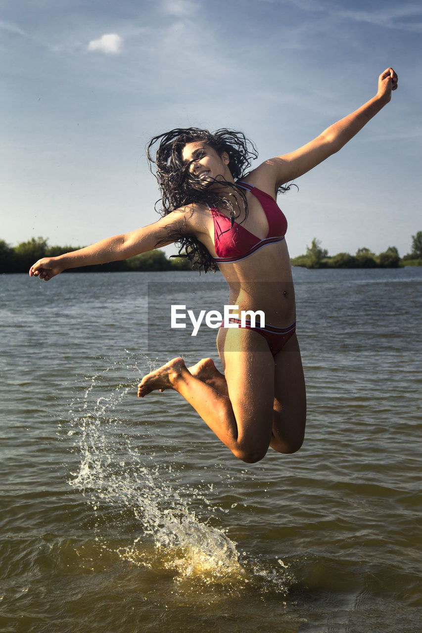 Full length of teenage girl wearing bikini jumping in lake