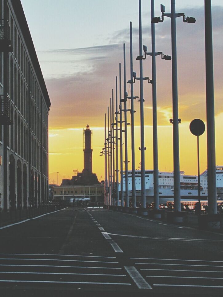 Street lamps on city street by building during sunset