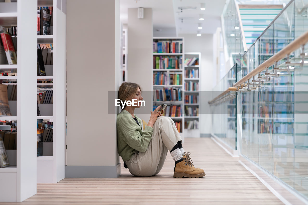 Middle aged student woman sitting on floor reading book in university library. second degree.