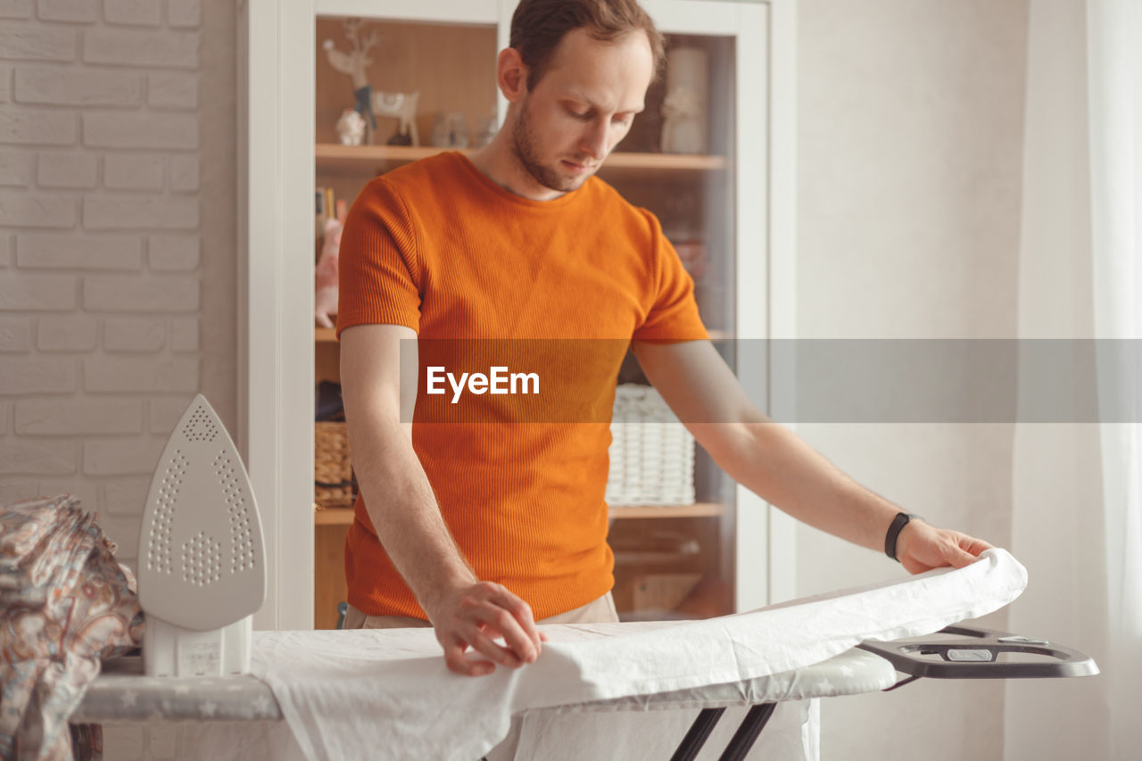 MAN LOOKING AT CAMERA WHILE STANDING ON BED