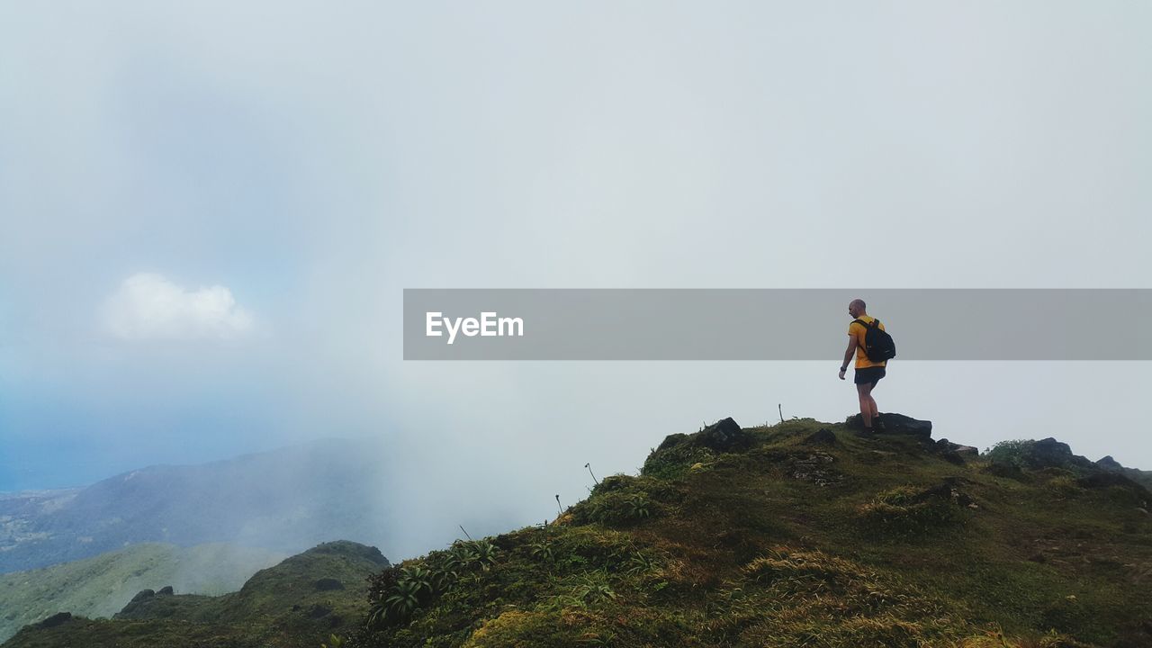 MAN STANDING ON MOUNTAINS AGAINST SKY