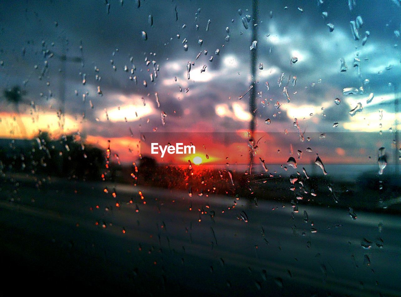 CLOSE-UP OF WET GLASS WINDOW AGAINST SKY DURING RAINY SEASON