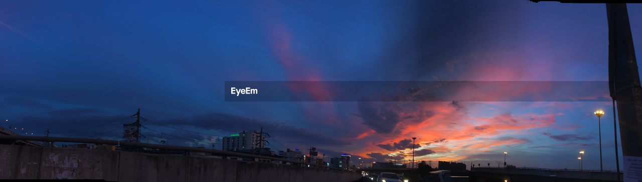 LOW ANGLE VIEW OF ILLUMINATED CITY AGAINST SKY AT SUNSET