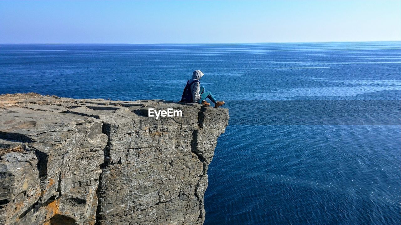 Side view of man on cliff against blue sky