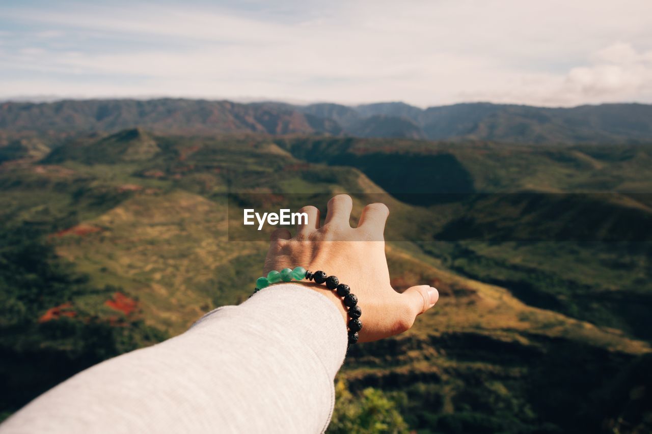 Close-up of man hand gesturing towards mountain against sky