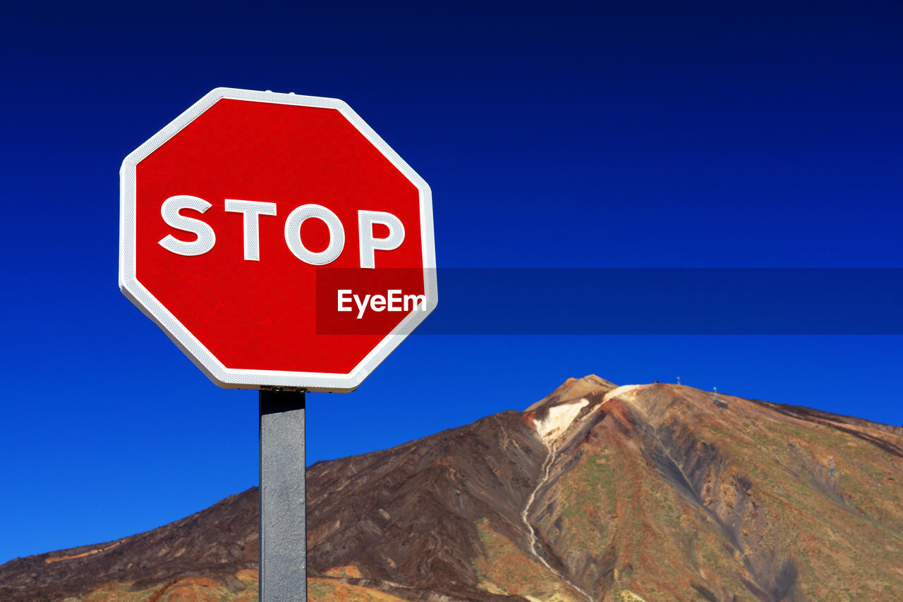 Low angle view of stop sign by rocky mountain at el teide national park against clear blue sky