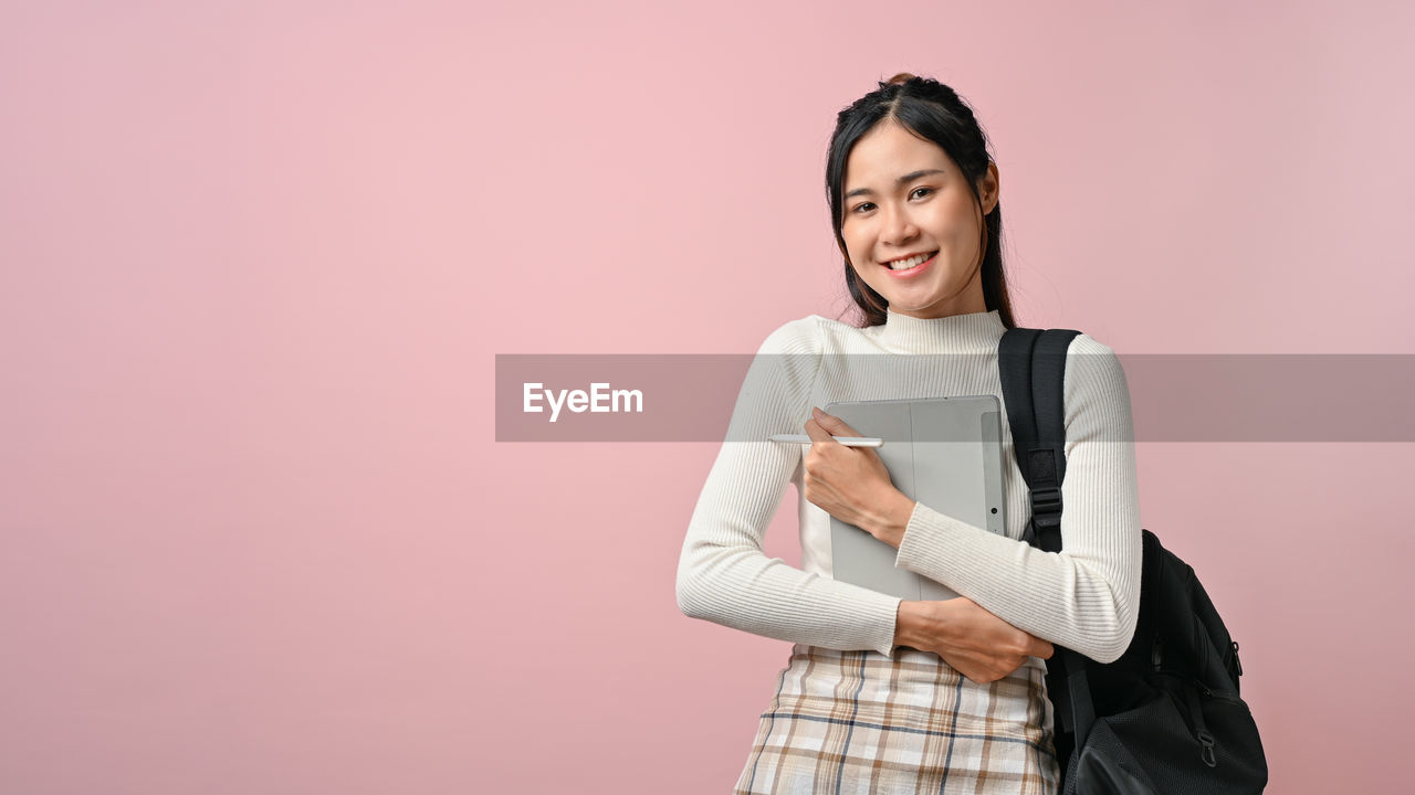 portrait of smiling young woman standing against wall