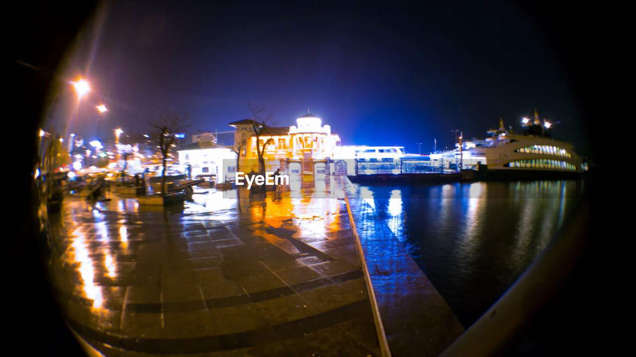 BOATS MOORED IN ILLUMINATED CITY AT NIGHT