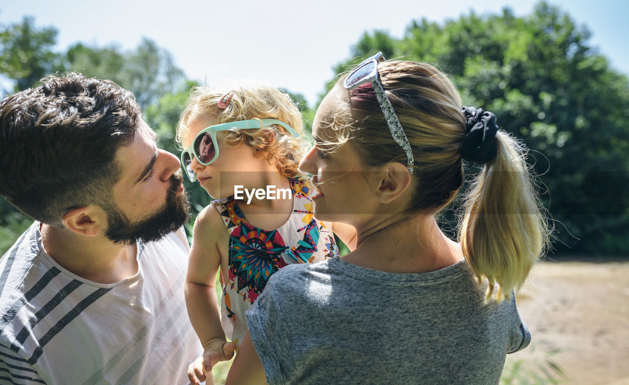 Little girl with sunglasses giving kisses to her parents