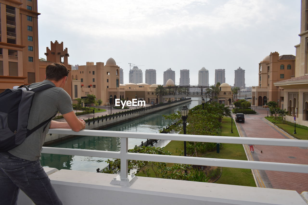 Rear view of man standing by the river against buildings in city