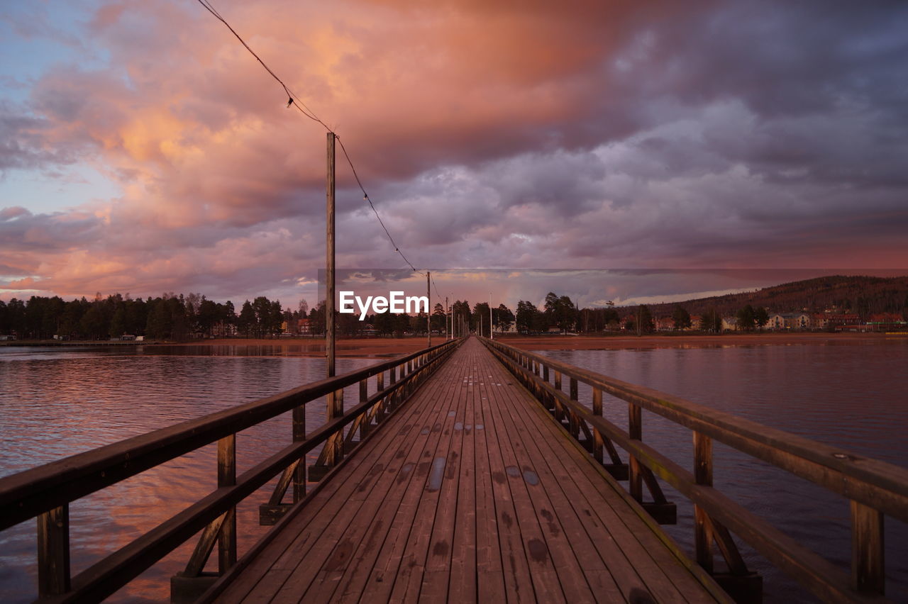 Footbridge on river against cloudy sky