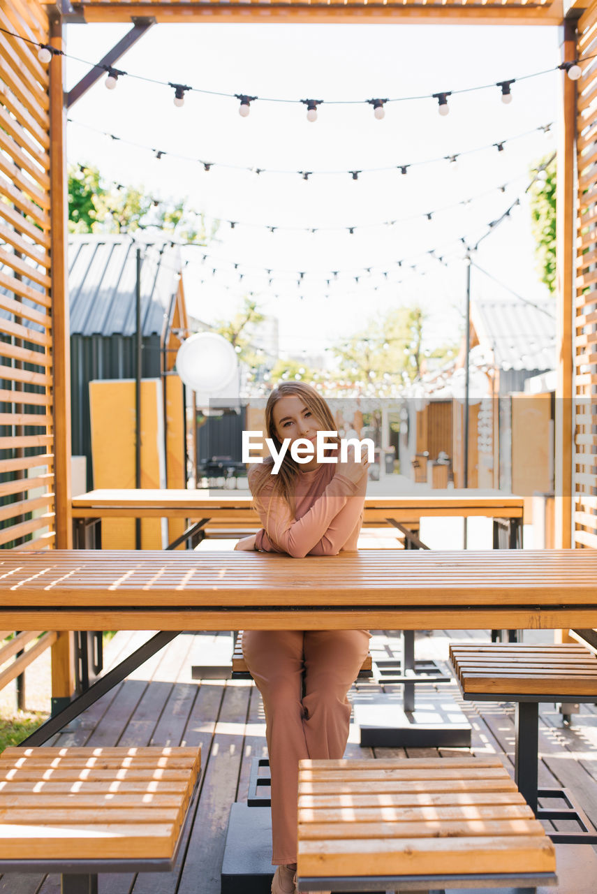 Happy charming young woman is sitting at a table in an outdoor cafe and waiting for her order person