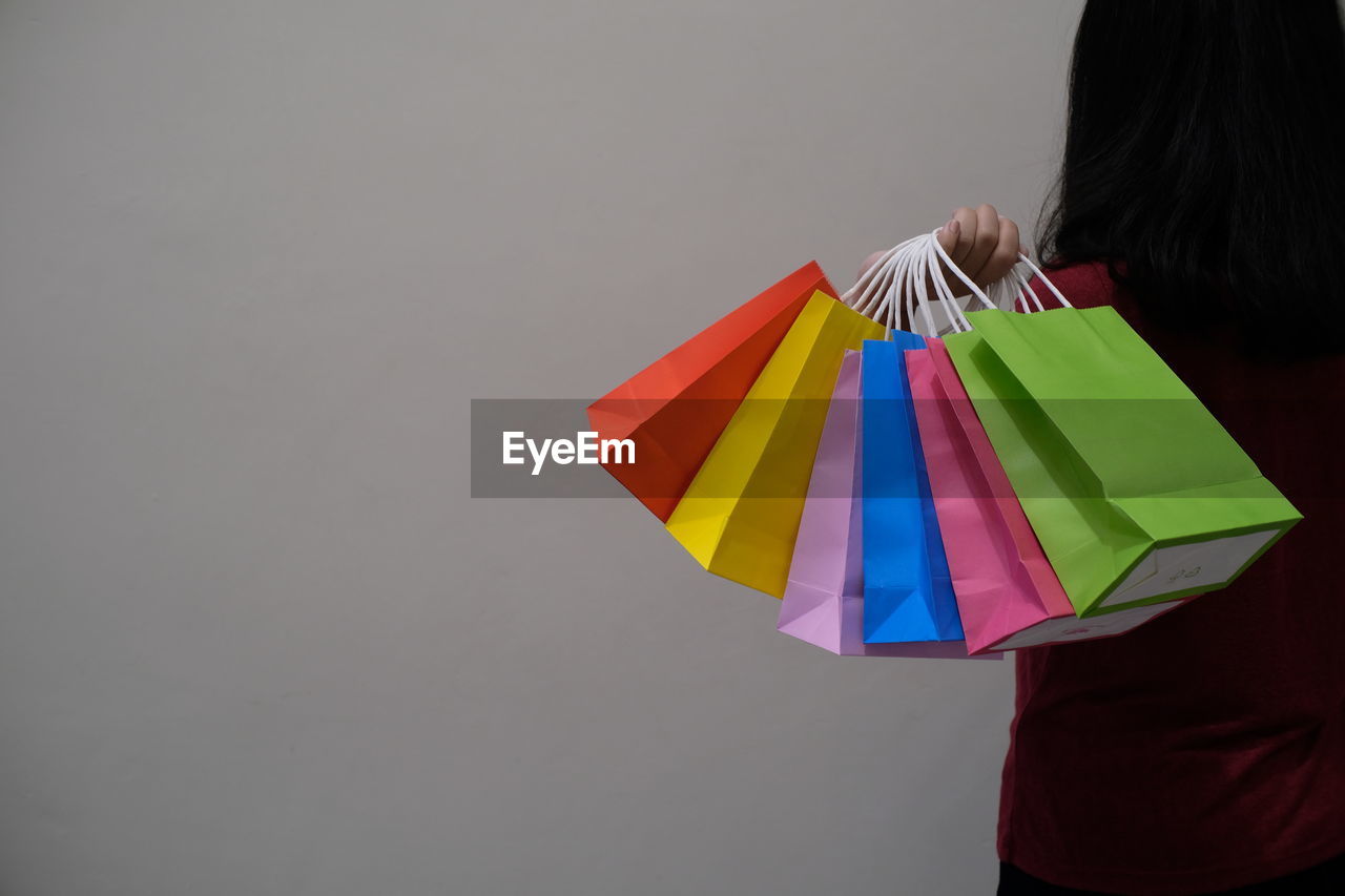 Rear view of woman holding colorful shopping bags against gray background