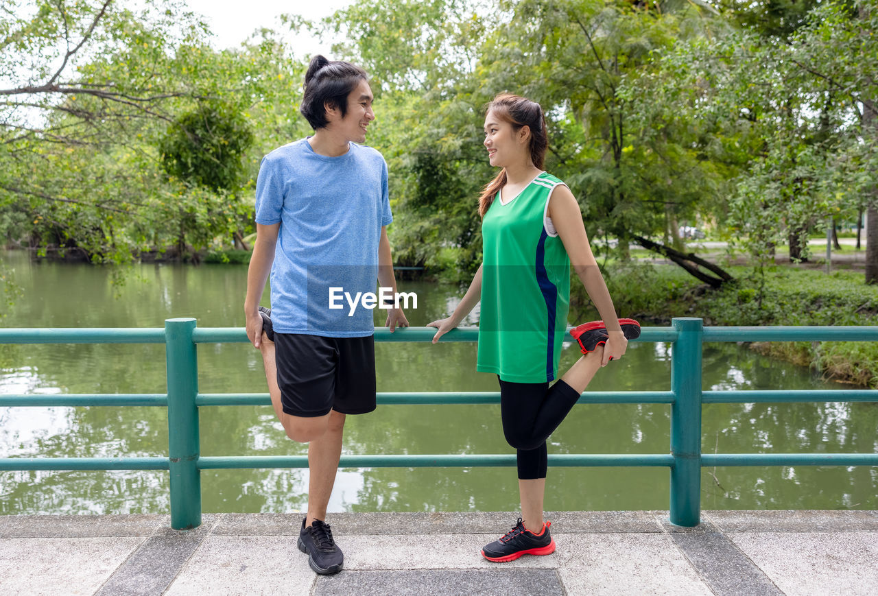 Outdoors on the bridge, an attractive young fitness couple stretching, a sporty guy and woman